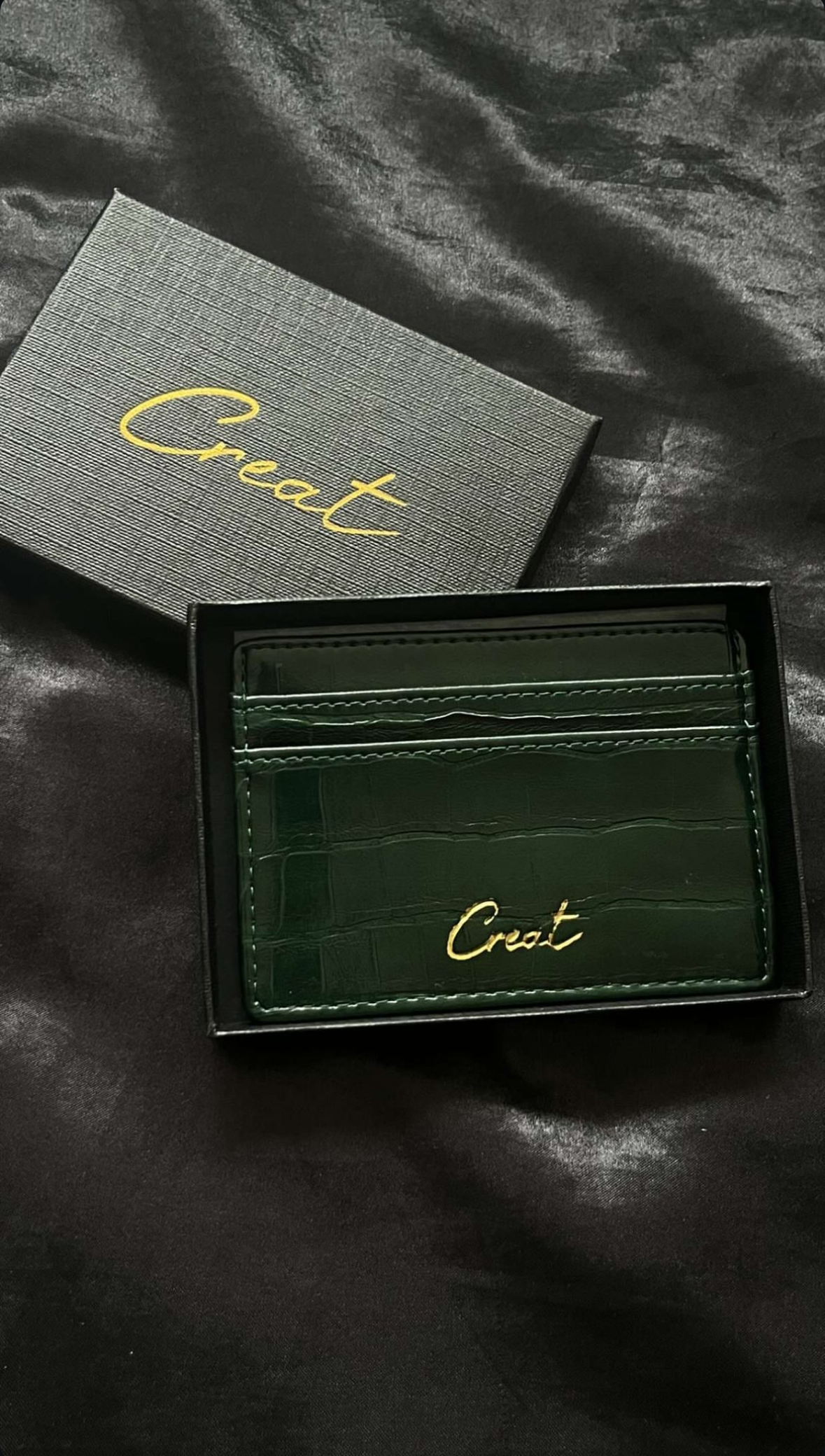 Green leather wallet with 'Creat' branding on a dark textured surface